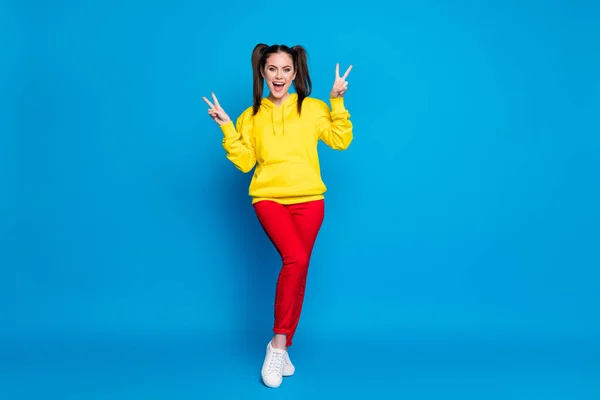 Foto de longitud completa de la señora bonita dos colas peinado mostrando símbolos de signo v buen humor decir hola amigos usan sudadera casual sudadera con capucha amarilla pantalones rojos zapatillas aisladas de color azul brillante fondo — Foto de Stock