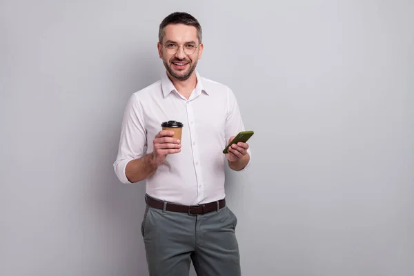 휴대 전화 웹 5g 연결 서비스를 사용하여 밝은 회색 파스텔 색 배경에 분리 된 카카오를 마시는 그의 매력적 인 유쾌하고 성숙 한 남자의 모습 — 스톡 사진