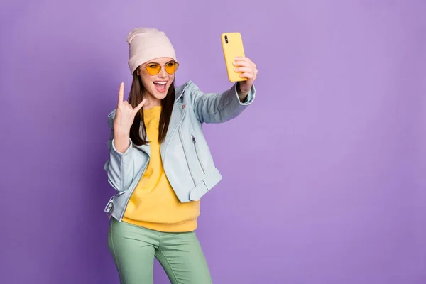 Foto de engraçado muito legal jovem senhora segurar telefone fazer selfies blogger popular mostrando chifres de dedo usar sol especificações casuais chapéu casaco amarelo pulôver calças isolado roxo cor fundo — Fotografia de Stock