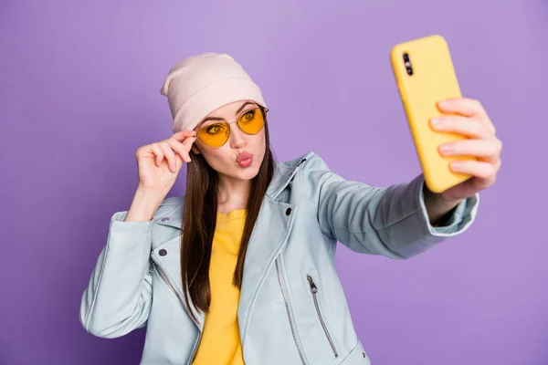 Foto di divertente bella giovane signora tenere il telefono fare selfie blogger popolare invio di baci d'aria indossare specifiche del sole casual cappello giacca giallo pullover isolato colore viola sfondo — Foto Stock