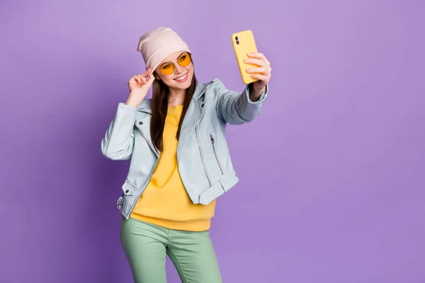 Foto van stijlvolle vrij mooie dame hold telefoon glimlachen make selfies volgelingen populaire blogger dragen zon specs casual hoed blauwe jas pullover groene broek geïsoleerde paarse kleur achtergrond — Stockfoto
