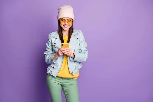Photo of cool stylish pretty lady street look clothes hold telephone chatting toothy smiling wear sun specs casual hat blue jacket yellow pullover green pants isolated purple color background — Stock Photo, Image