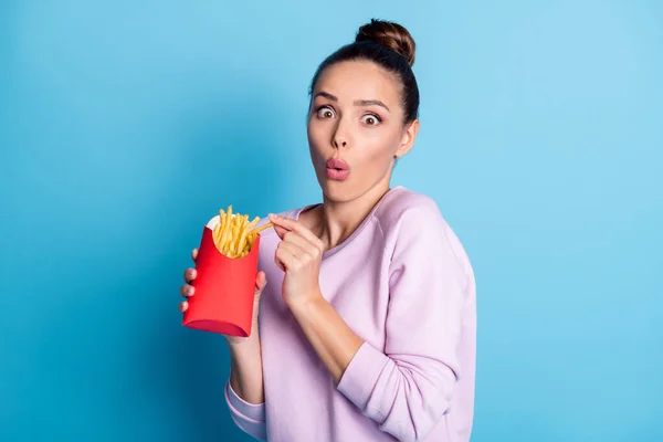 Foto av förvånad flicka äta hämtmat krispiga pommes frites imponerad skräpmat läckra mellanmål bära lila pullover isolerad över blå färg bakgrund — Stockfoto