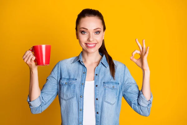 Retrato de positivo alegre menina promotor de café segurar xícara com show de cacau quente sinal ok recomendo beber desgaste roupa boa aparência isolada sobre fundo de cor brilhante — Fotografia de Stock