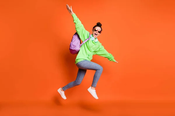 Фотографічний портрет школярки, що робить літак з руками, стрибає вгору ізольовано на яскраво-помаранчевому фоні — стокове фото
