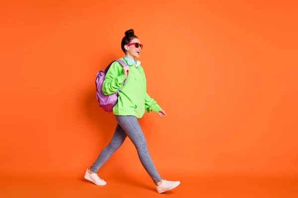 Foto de comprimento total de caminhada jovem senhora vestida mochila camisola verde olhando espaço vazio isolado cor laranja brilhante fundo — Fotografia de Stock