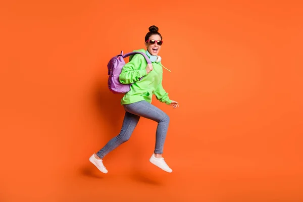 Volledige lengte foto van vrolijke jonge vrouw dragen groene hoodie schooltas bril lopen geïsoleerde levendige oranje kleur achtergrond — Stockfoto