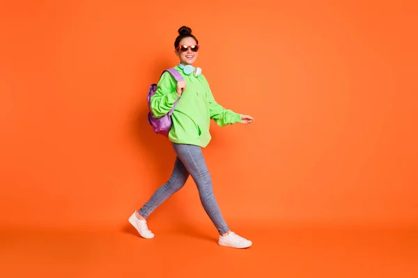 Foto de comprimento total de mulher andando adorável usar óculos saco de escola com capuz verde isolado fundo de cor laranja vívida — Fotografia de Stock