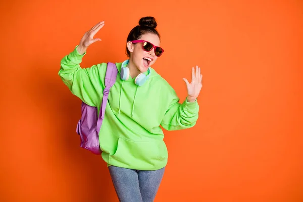 Dans eden genç bir kadının fotoğrafı yeşil kapüşonlu okul gözlüğü takıyor kollarını kaldırıyor turuncu renkli arka plan. — Stok fotoğraf