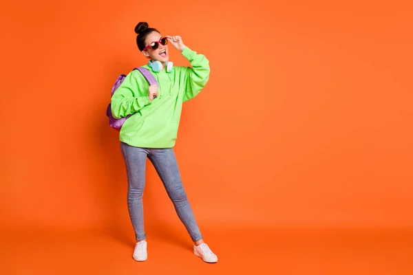 Foto de bonito jovem mulher usar óculos saco de escola com capuz verde olhando espaço vazio isolado vívida cor de fundo laranja — Fotografia de Stock