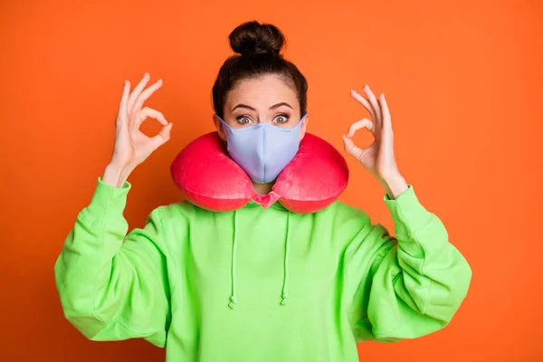 Foto da jovem mulher usar verde com capuz pescoço travesseiro máscara médica mostrando okey sinal isolado vívido cor laranja fundo — Fotografia de Stock