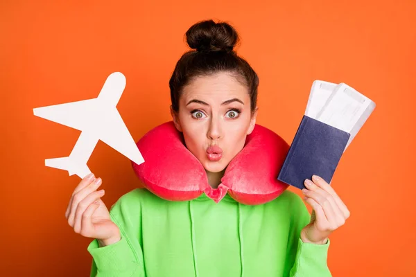 Foto de señora divertida vestida sudadera verde cuello almohada labios pucheros celebración de billetes de avión aislados de color naranja brillante fondo —  Fotos de Stock