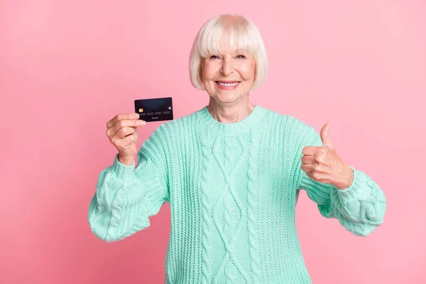 Fotoporträt einer Rentnerin mit blonden Haaren, die ihre Kreditkarte lächelnd hält, die wie eine aufgeblasene Geste auf pastellrosa Hintergrund erscheint — Stockfoto