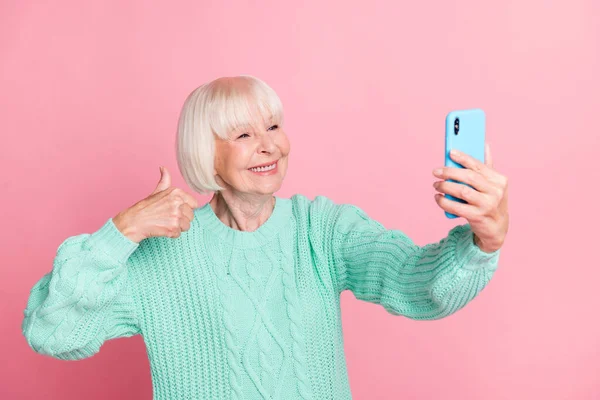 Şirin bir büyükannenin selfie çekerken çekilmiş fotoğrafı başparmak kaldırma işareti gibi, pastel pembe arka planda izole edilmiş. — Stok fotoğraf