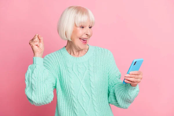 Meraklı yaşlı bir kadının fotoğrafı internette geziniyor kazanan gibi el kol hareketi yapıyor evet diye bağırıyor pastel pembe arka planda izole edilmiş. — Stok fotoğraf