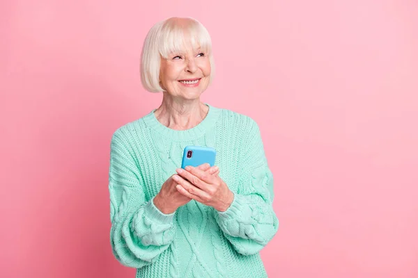 Foto ritratto di curiosa donna anziana utilizzando il cellulare guardando lo spazio vuoto isolato su sfondo rosa pastello — Foto Stock