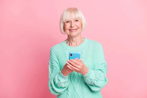 Cep telefonu kullanan neşeli yaşlı bir kadının fotoğrafı. Gülümseyen bir mesaj. Pastel pembe arka planda izole edilmiş. — Stok fotoğraf