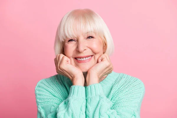 Foto retrato de encantadora mujer mayor en suéter verde azulado pelo rubio sonriente tocando mejillas aisladas sobre fondo de color rosa pastel — Foto de Stock