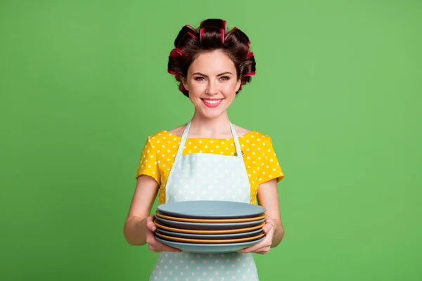 Foto di positivo cameriera ragazza lavare i piatti dopo la famiglia raccolta tenere pila usura giallo punteggiato abito capelli rulli isolato su sfondo di colore verde — Foto Stock