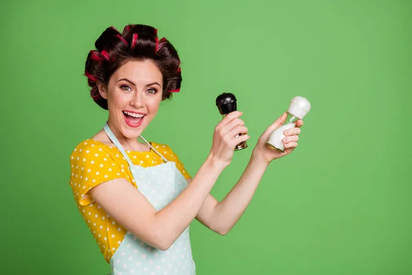 Photo of pretty cute girlish young lady roller hairstyle hold pepper shaker salt bottle open mouth pretend mexican dancer wear dotted apron shirt isolated green color background — Stock Photo, Image