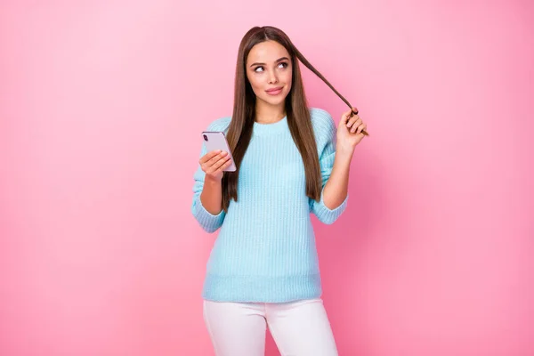 Фото красивої блогера леді тримає телефон, щоб порожній простір написати новий пост рани завиток навколо пальця в'язаний синій светр білі штани ізольовані пастельно-рожевий кольоровий фон — стокове фото