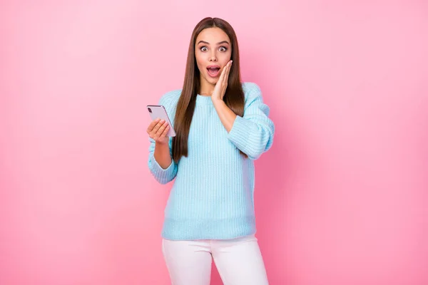 Фото довольно шокированы леди руку на щеку держать телефон проверки последователей многие любят комментарии носить вязаный синий свитер белые брюки изолированные пастельно-розовый цвет фона — стоковое фото