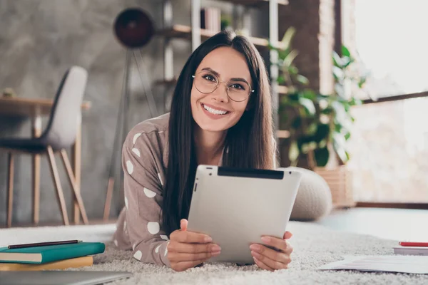 Foto de chica optimista agradable mintiendo escribir tableta usar gafas pijama en casa —  Fotos de Stock