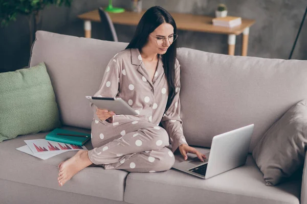 Fotografie pěkně optimistické dívky sedět psát laptop hold tablet nosit brýle pijama doma na pohovce — Stock fotografie