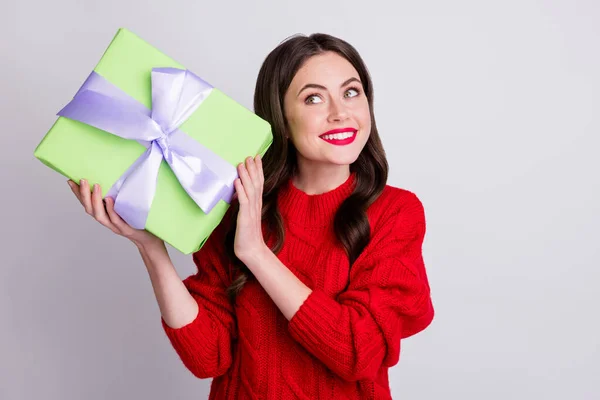 Photo portrait of curious interested woman trying to guess whats inside gift box smiling isolated on pastel grey color background