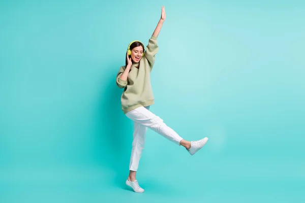 Retrato fotográfico completo de una mujer guay con auriculares verdes bailando de pie sobre una pierna aislada sobre un fondo vivo de color turquesa —  Fotos de Stock