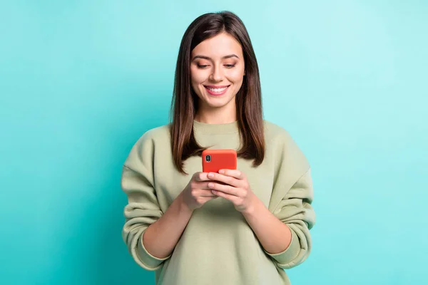 Фотопортрет улыбающейся женщины, печатающей телефон в двух руках, изолированный на ярком бирюзовом фоне — стоковое фото