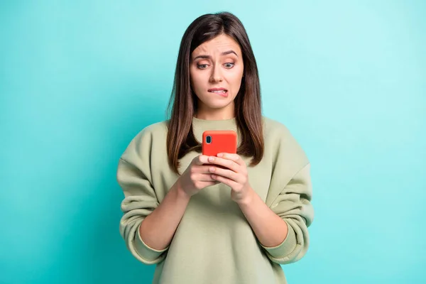 Foto retrato de menina mordendo lábio inferior segurando telefone em duas mãos isoladas em fundo colorido turquesa vívida — Fotografia de Stock