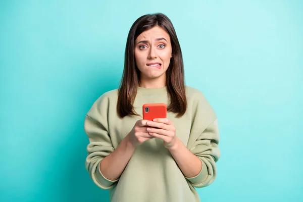 Foto portret van angstige vrouw bijten onderlip holding telefoon in twee handen geïsoleerd op levendige teal gekleurde achtergrond — Stockfoto