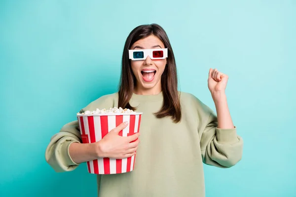 Photo portrait of screaming girl in 3d glasses holding large popcorn bucket with raised fist isolated on vivid turquoise colored background — Stock Photo, Image