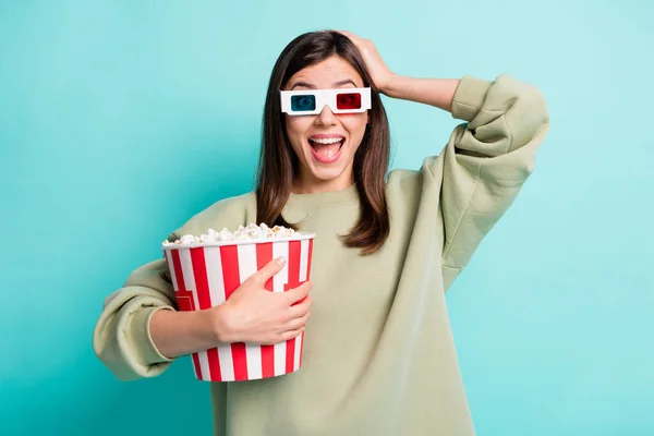 Photo portrait of shocked woman in 3d glasses touching head holding giant popcorn bucket in one hand isolated on vivid teal colored background — Stock Photo, Image