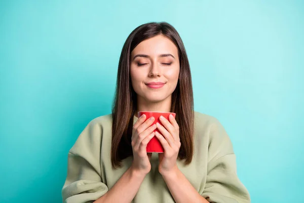 Foto retrato de mujer inhalando aroma de café agradable sosteniendo taza roja en dos manos con los ojos cerrados aislados sobre fondo vivo de color turquesa — Foto de Stock
