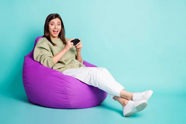 Foto potret seluruh tubuh gambar dari teriakan wanita yang bersemangat bermain game dengan pengendali duduk di kursi ungu terisolasi di latar belakang berwarna cerah — Stok Foto