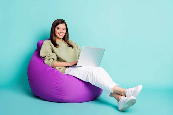 Potret potret seluruh tubuh gadis yang bekerja pada laptop duduk di kursi berlengan beanbag ungu terisolasi pada latar belakang berwarna cerah — Stok Foto
