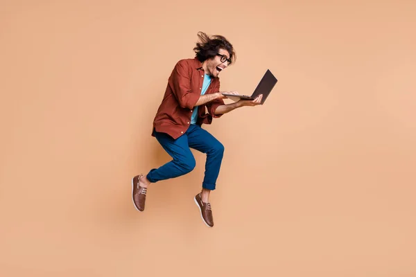 Photo portrait widok całego ciała krzyczący facet skaczący z laptopem w rękach odizolowany na pastelowym beżowym tle — Zdjęcie stockowe