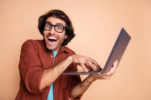Фотографічний портрет божевільного хакера, який тримає ноутбук в руці ізольовано на пастельному бежевому фоні — стокове фото