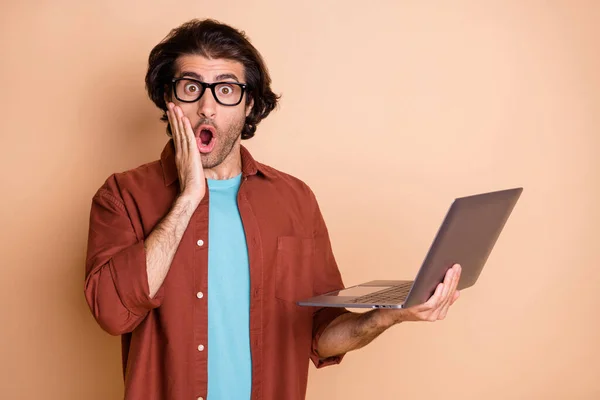 Foto portret van geschokte man aanraken gezicht wang houden laptop in de hand geïsoleerd op pastel beige gekleurde achtergrond — Stockfoto