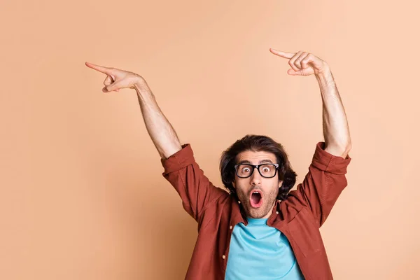 Foto de loco sorprendido dedo directo espacio vacío boca abierta usar gafas marrón camiseta aislado color beige fondo —  Fotos de Stock