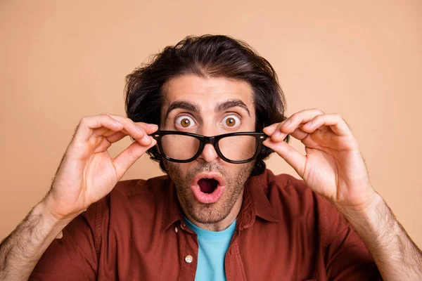 Photo of crazy surprised young man fingers hold glasses open mouth wear spectacles brown t-shirt isolated beige color background — Stock Photo, Image