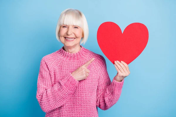 Foto retrato de mulher velha apontando dedo em segurar cartão de coração em uma mão isolada no fundo de cor azul pastel — Fotografia de Stock