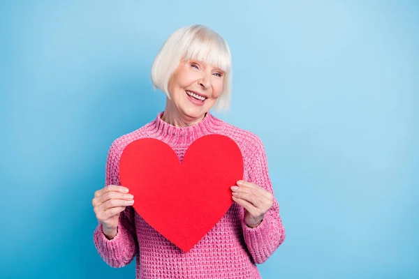 Fényképezés portré aranyos idős hölgy kezében piros szív képeslap két kézzel elszigetelt pasztell kék színű háttér — Stock Fotó