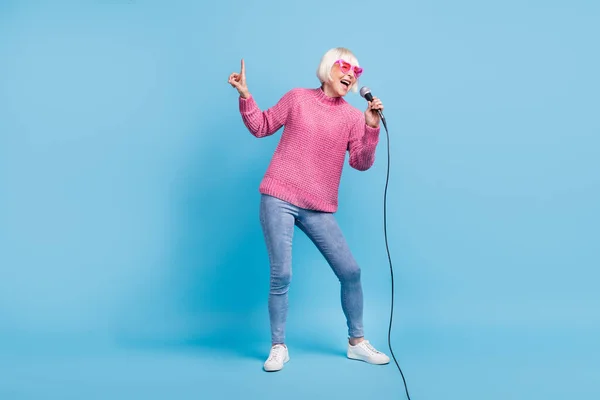 Foto retrato vista de corpo inteiro de idosa senhora cantando apontando dedo para cima segurando microfone em uma mão isolada no fundo de cor azul pastel — Fotografia de Stock