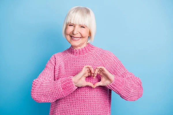 Mutlu, yaşlı bir kadının göğsünde parmakları olan kalbi gösteren fotoğrafı. Pastel mavisi arka planda izole edilmiş. — Stok fotoğraf