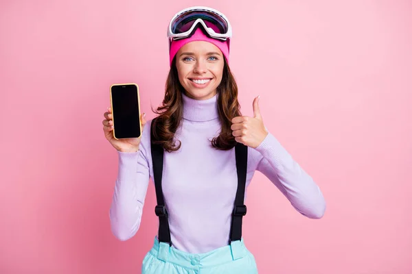 パステルピンク色の背景に孤立した片手で空白のディスプレイを持つ電話を持って親指を示す女性の写真肖像画 — ストック写真