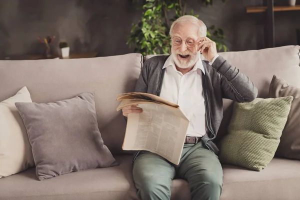 养老金领取者笑着穿着灰色羊毛衫坐在沙发上看报纸的照片 — 图库照片