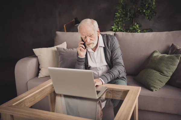 Photo of angry pensioner wear grey cardigan sitting looking modern gadget talking phone indoors house flat — Stock Photo, Image